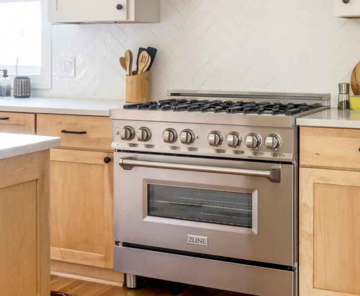A stainless steel professional-style gas range with six burners in a kitchen with light wood cabinets and white countertops.