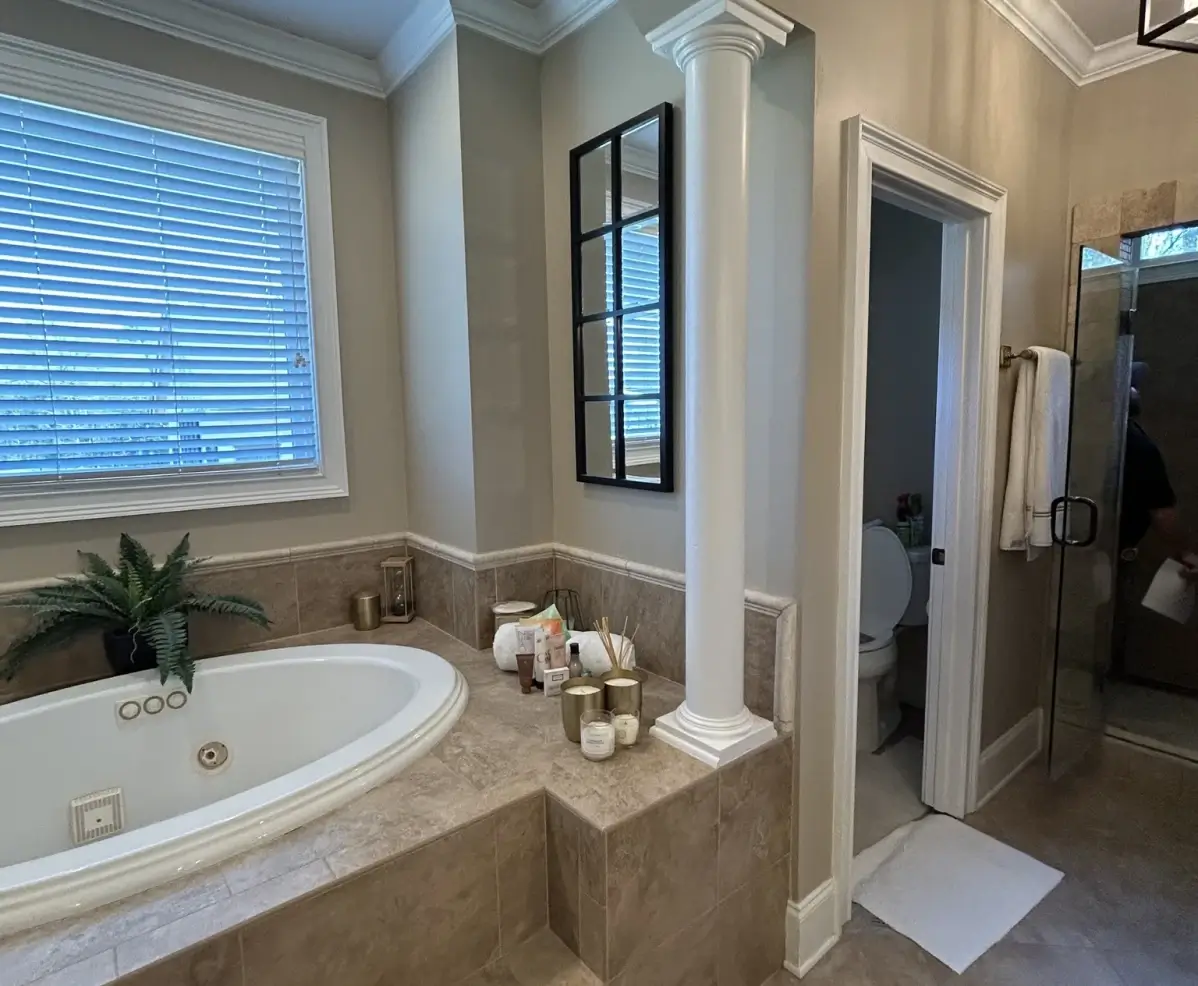 A luxury bathroom with a corner soaking tub, beige tile surround, a window with blinds, and an adjacent walk-in shower.