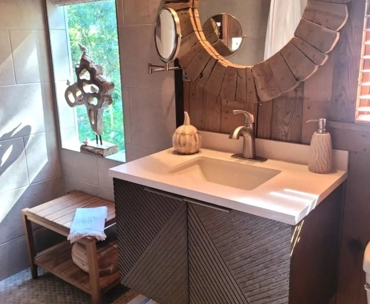 A modern bathroom vanity with a textured gray cabinet, white countertop sink, round mirror, and hexagonal tile wall.