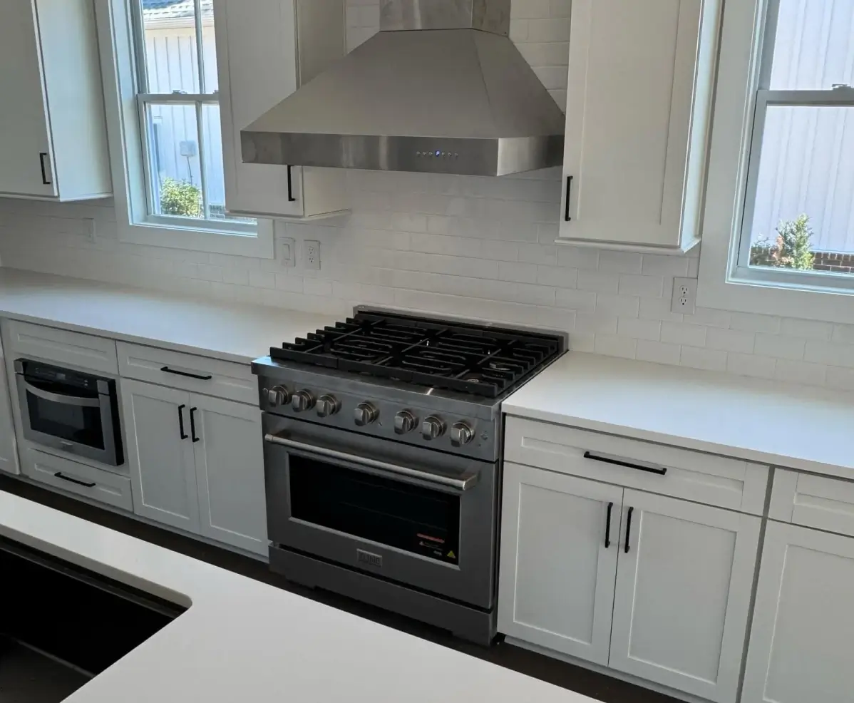 A white kitchen with shaker cabinets, a stainless steel range hood, a gas stove, and windows on either side.