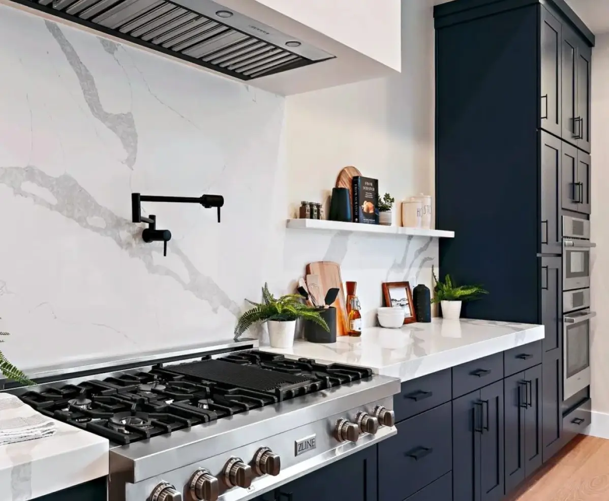 A modern kitchen with navy blue cabinets, a white marble backsplash, a gas stove, and open shelving with decorative items.