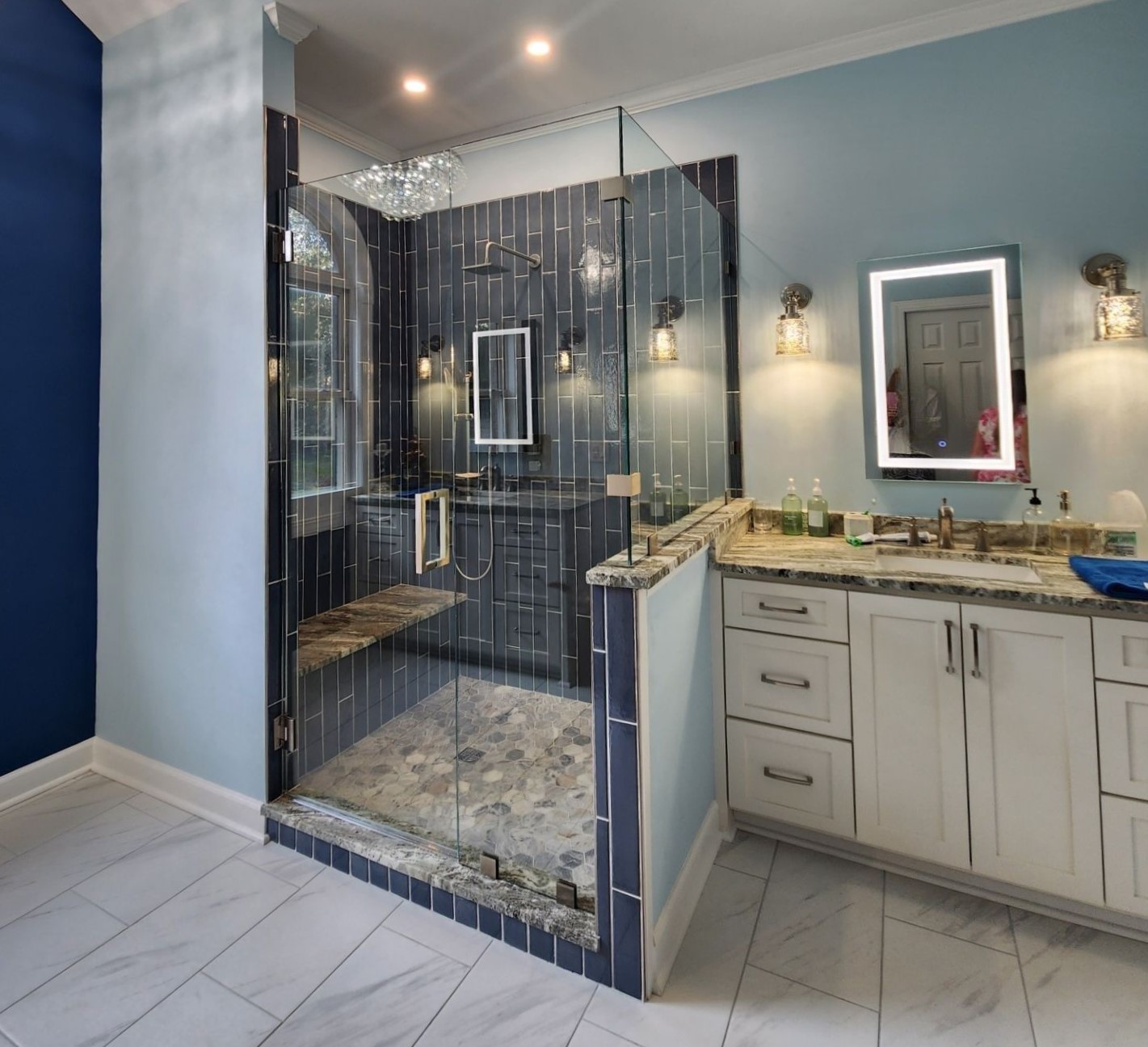 Bathroom renovation with glass shower, blue tile, double vanity, mirrors, and wall sconces.