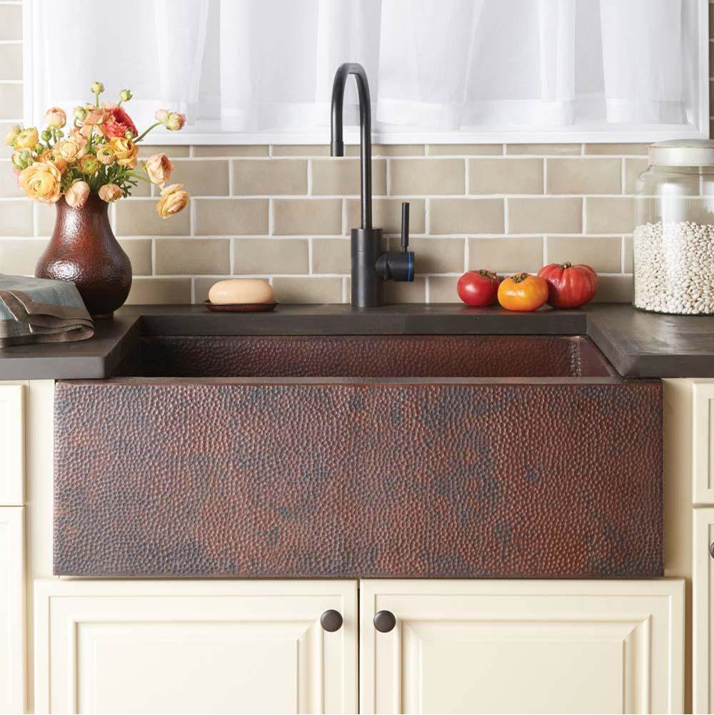 Bath and Bronze copper apron-front kitchen sink with black faucet, cream cabinets, and subway tile.