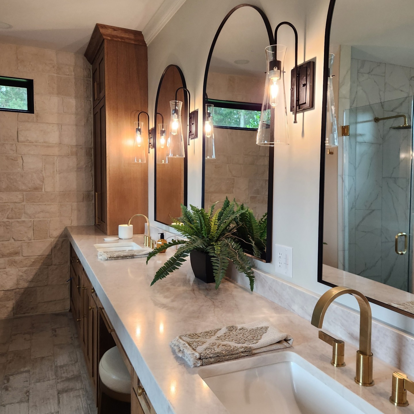 Modern bathroom vanity with marble countertop, brass fixtures, arched mirrors, and wall sconces for soft lighting.