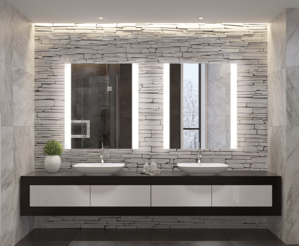 Modern double vanity bathroom with backlit mirrors, stone wall, and sleek vessel sinks under soft lighting.