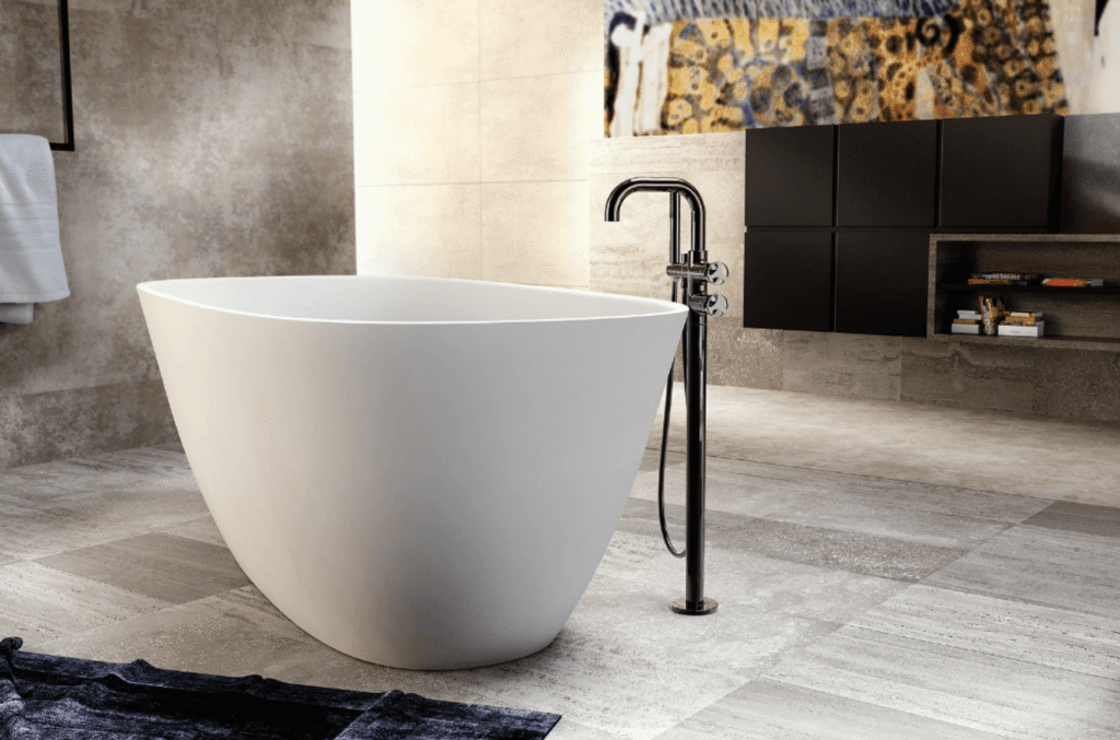 Modern freestanding bathtub with floor-mounted faucet in a neutral-toned bathroom with textured walls and shelving.