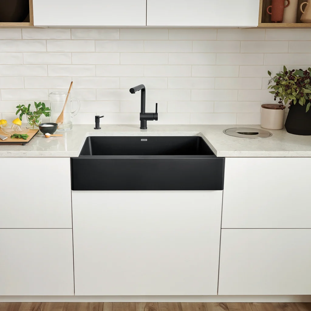 Black apron-front kitchen sink with matte black faucet, white cabinets, and subway tile backsplash.